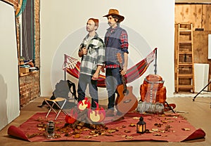 Serious, attentive look. Two men imagining, recreating camping activity indoors with necessary equipment. Concept of