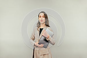 Serious attractive woman with a laptop in her hands stands on a beige background and poses for the camera, staring intently.