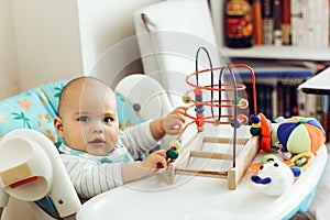 Serious baby boy playing toys in high chair at home