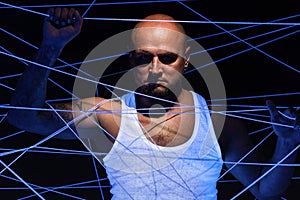 Serious bald man tangled in threads in ultraviolet