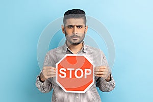 Serious bearded businessman holding Stop road traffic sign as symbol of prohibition, restrictions.