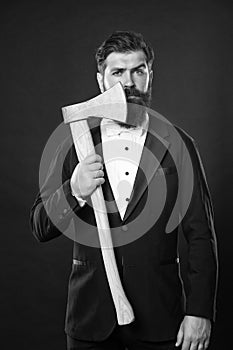 Serious bearded man in formal suit holding hatchet at unshaven face dark background, barbershop