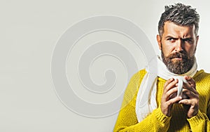 Serious bearded man in knitted sweater and scarf with cup of hot coffee or tea. Autumn or winter time. Handsome male in