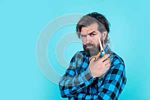 serious bearded man with scissors on blue background with copy space, hairdresser salon