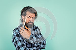 serious bearded man with scissors on blue background with copy space, hairdresser salon