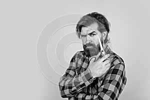 serious bearded man with scissors on blue background with copy space, hairdresser salon