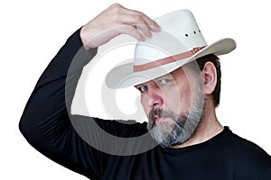 A serious bearded middle-aged man puts on a cowboy hat