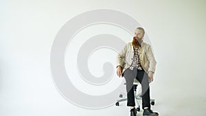 Serious bearded man sitting on swivel office chair and looking into camera on white background