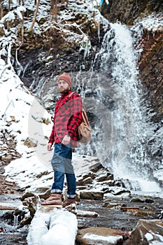 Serious bearded young man standing near mountain waterfall in winter