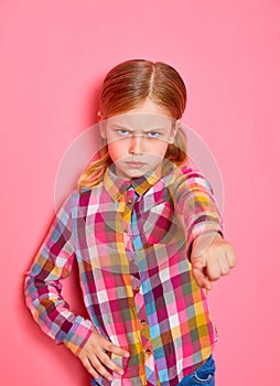 Serious beautiful little girl pointing a finger at you on pink background.