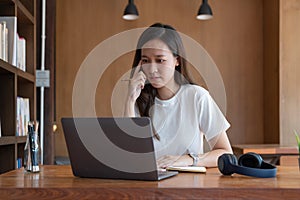 Serious beautiful woman with hand on chin sitting near while looking at open laptop computer on table.