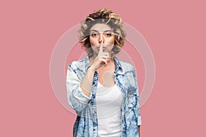 Serious beautiful woman standing with finger near lips, showing shh gesture, keep silence.