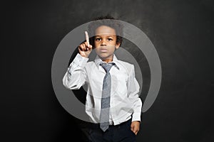 Serious black child student boy pointing up on black, portrait