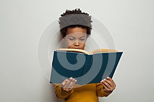 Serious black kid boy reading a book on white background