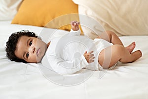 Serious black little child girl or boy in clothes lies on white comfort bed in bedroom. Health care, newborn