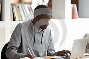 Serious black male student using laptop, busy with studying.