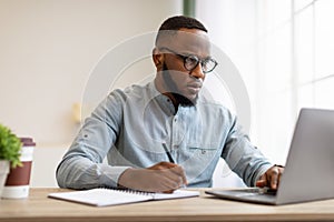 Serious Black Man Writing Business Report At Laptop In Office