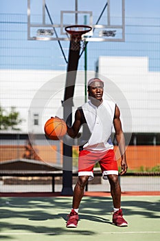 Serious black sportsman dribbling ball at basketball court outdoors