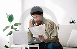 Serious black teen guy studying online from home, talking to his tutor about coursework paper on smartphone