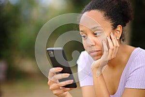 Serious black woman using cell phone in a park