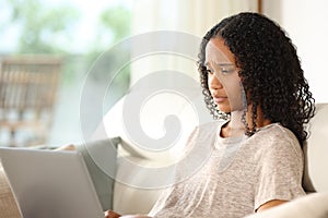 Serious black woman using laptop in a house interior