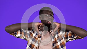 Serious black young millennial man shows refusal gesture with thumbs down disagree negative standing at blue background