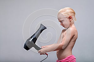 Serious blond boy with wet hair is blow dry. White background