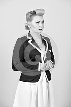 Serious blonde girl in jacket looks up. Woman in pin-up style dressed in jacket on grey