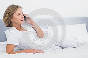 Serious blonde woman lying on bed making a phone call