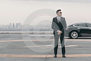 serious bodyguard standing with sunglasses and security earpiece on helipad and looking