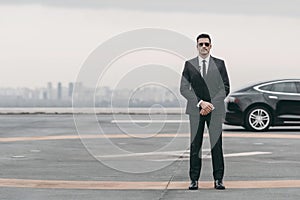 serious bodyguard standing with sunglasses and security earpiece on helipad and looking photo