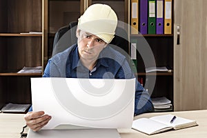 Serious boss in hard hat at his desk examines the project documentation. Builder, engineer, proctor, foreman