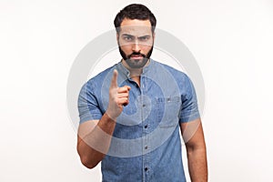 Serious bossy man with beard in blue shirt warning with finger, scolding, strictly looking at camera