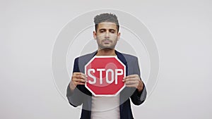 Serious bossy man holding and showing red stop traffic sign, warning and asking to be attentive, speed limit, keeping traffic laws