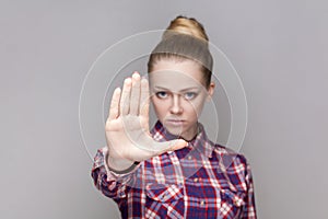 Serious bossy woman with bun hairstyle showing prohibition gesture, shows stop palm sign.