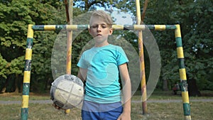 Serious boy with football looking into camera at football pitch, street match