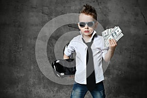 Serious boy little businessman in white shirt, jeans, tie and sunglasses standing and holding toy car present and dollars cash