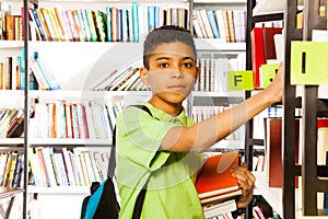 Serious boy looks and searches book on shelf