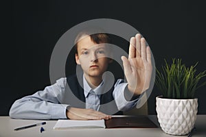 Serious boy showing stop sign sittin isolated in the class.