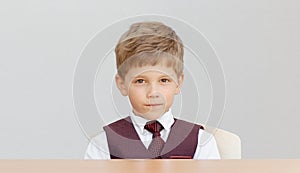 Serious boy sits at the desk in a vest with a tie