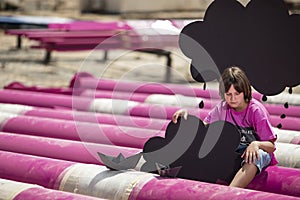 Serious boy sits on a pink pipes with black paper boats and clouds at the construction site