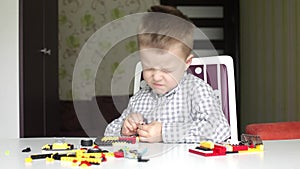 Serious boy trying to detach bricks of children's building kit