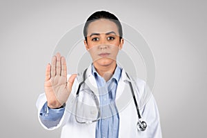 Serious brazilian lady doctor doing stop gesture with hand, fight against disease, professional advice, no sign