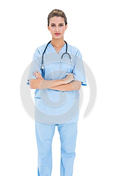 Serious brown haired nurse in blue scrubs posing with arms folded