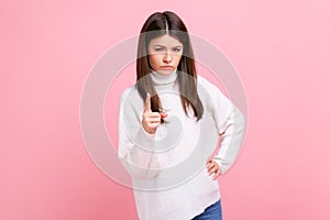 Serious brunette female standing with raised index finger, warning you, looking seriously at camera.