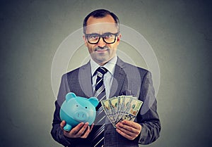 Serious business man in glasses with piggy bank and dollar cash banknotes