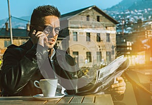 Serious business man with newspaper and coffee talking by mobile