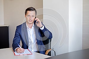 Serious business man in office making cell phone call and taking notes