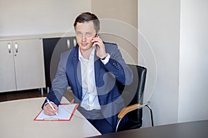 Serious business man in office making cell phone call and taking notes