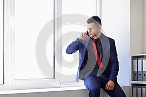 Serious business man talking on cell phone sitting on window sill